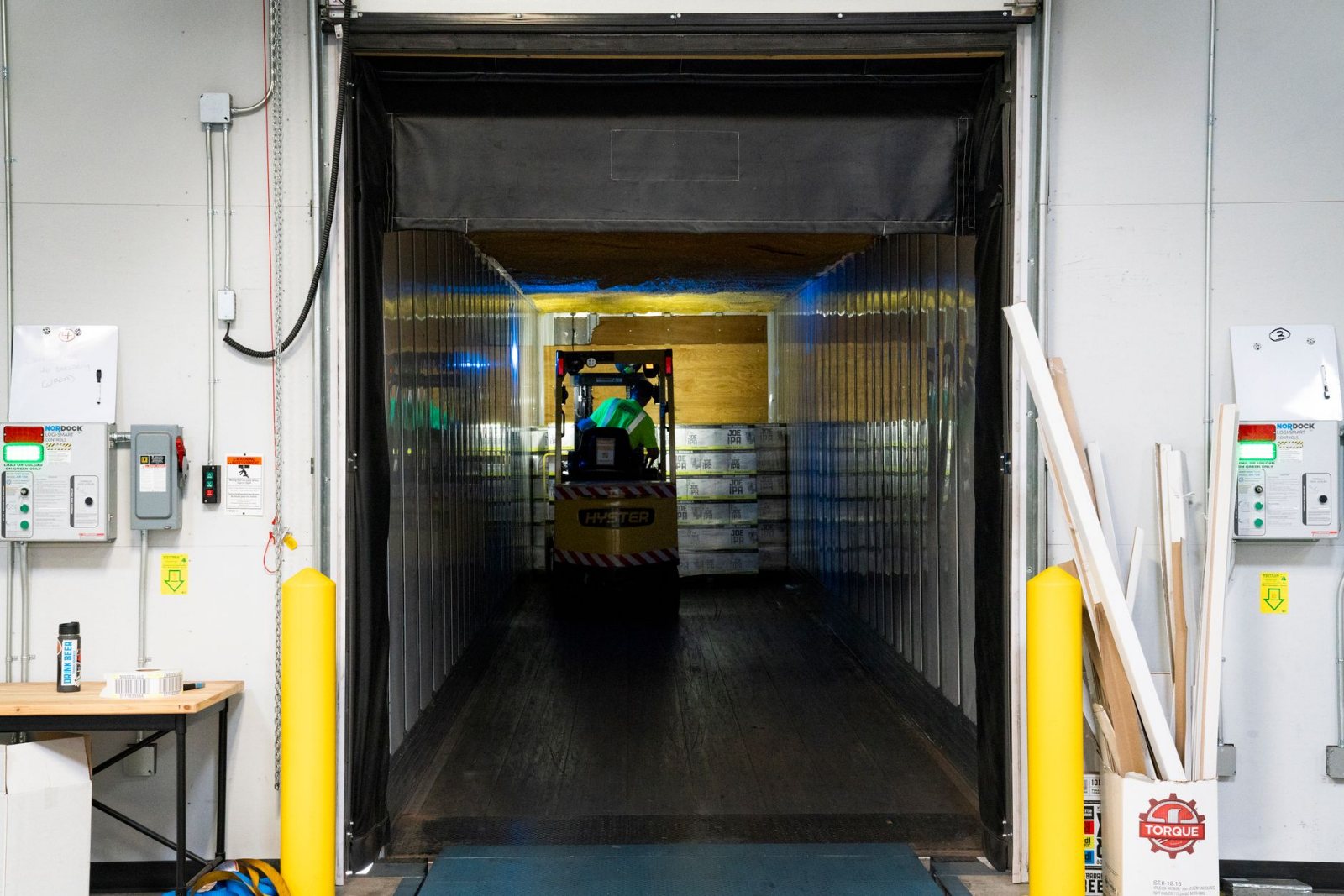 Shrink-wrapped freight coming off a trailer at a receiving dock on a pallet jack crossing the dock plate, a clipboard